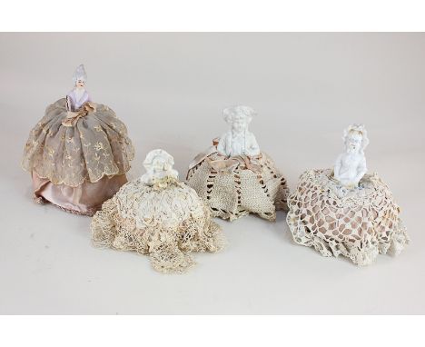 Four porcelain and bisque half dolls, each on pincushion base below lace, crochet and fabric skirts, tallest 17.5cm