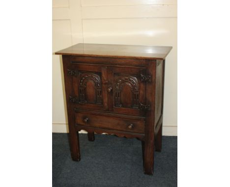 A small carved oak cabinet with two panel doors enclosing a cupboard and shelf above a single drawers, on rectangular block l