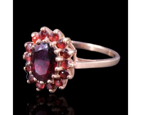 A garnet cluster ring, having a central oval-cut stone of approx 1.5 cts, gallery-claw set on a 9ct gold shank, R/S, 2.8 g