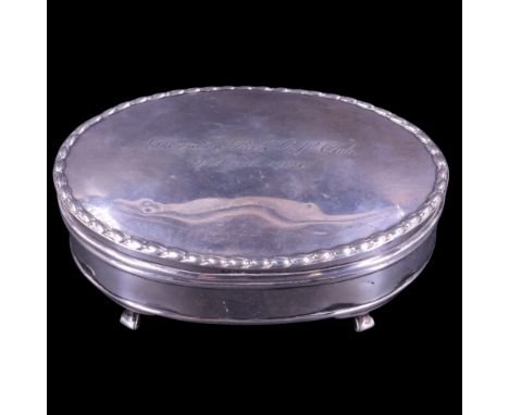 A 1920s silver ring or trinket box, of oval section raised on four scroll legs, its subtly domed hinged lid bordered with a h