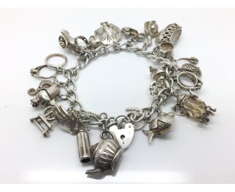 An early silver charm bracelet with 21 charms to include a fish, a teapot and a decorated peacock, heart clasp in working ord