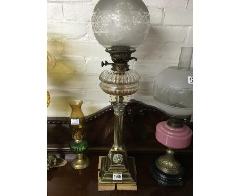 A Victorian brass oil lamp with glass shade a funnel the clear font above a collom on steeped base