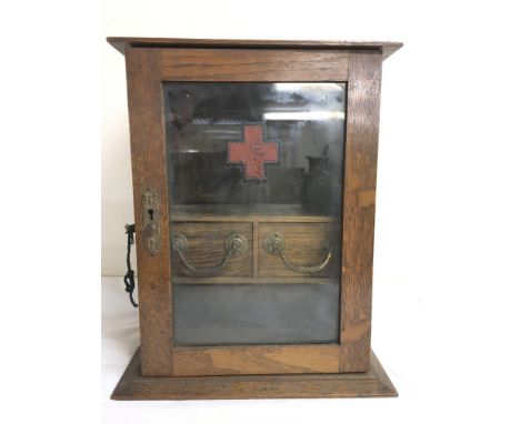 A wooden, glass panelled first aid box inset with shelf and two drawers, approximately 37cm tall x 24.5cm wide x 21cm deep.