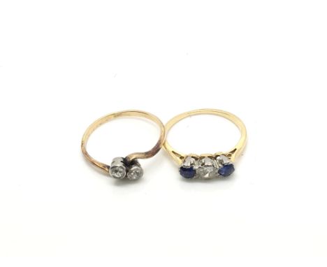 A yellow metal two stone crossover ring and a yellow metal three stone ring alternating between sapphires and white stones, r