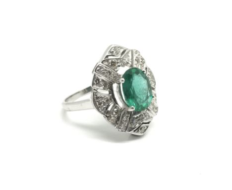 A ladies 14ct white gold ring inset with a central oval cut emerald in an Art Deco style, approximately 2ct, ornately surroun