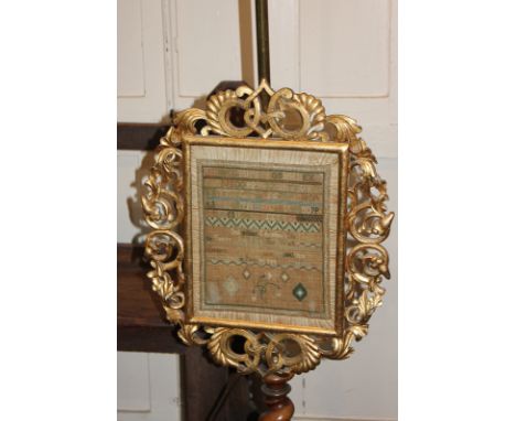 An alphabet sampler adjustable fire screen in gilt scroll frame with brass pole and turned wood support, on tripod base, now 