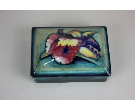 A Moorcroft pottery rectangular trinket dish and cover decorated with an orchid on blue and green ground, 13cm, (a/f)