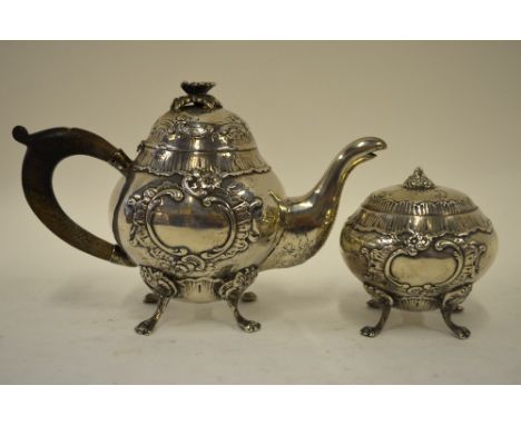 A German .800 grade bachelor teapot and sugar basin in the Rococo manner with embossed shell and scroll decoration and pad fe