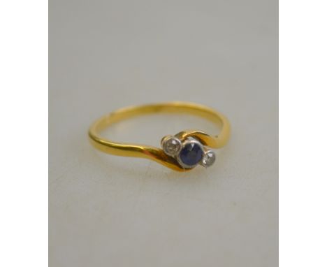 A sapphire and diamond three stone crossover ring, white metal millgrain setting with yellow metal shawl stamped 18ct