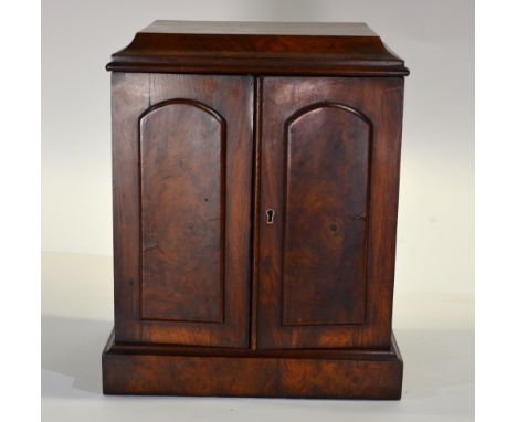 A Victorian figured walnut table cabinet having a caddy top over a pair of raised arched panel doors enclosing three graduate