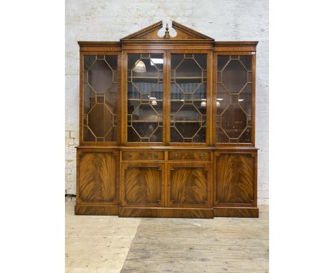 A Georgian style mahogany breakfront bookcase, the broken arch pediment with urn finial over dentil cornice and four astragal