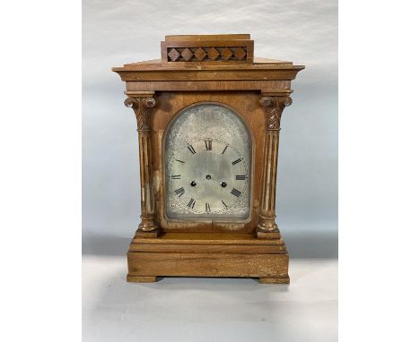 A large wooden mantle clock with Ionic columns either side of the dial, roman numerals, etched acanthus details surrounding d