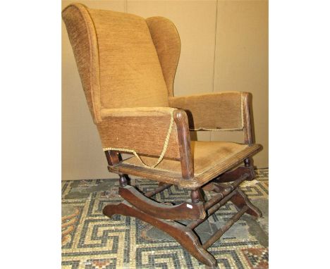 A vintage upholstered wing back sprung rocking chair with moulded and turned framework 