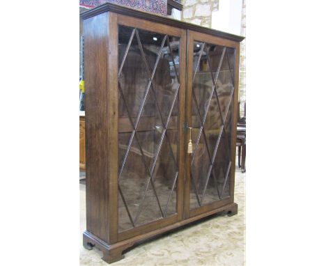 A Georgian style oak side cabinet freestanding and enclosed by a pair of rectangular astragal glazed panelled doors revealing