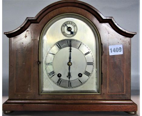 A good quality twin train walnut mantel clock of shaped form, arched silver dial with silver chapter ring and Roman numerals 