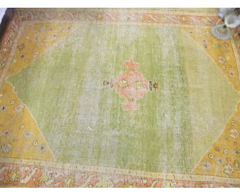 A Turkish rug, the central panel with a stylised lozenge shaped medallion on a green ground, within an orange floral decorate