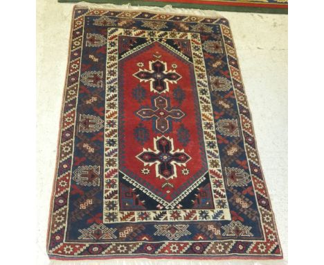 A Caucasian rug, the three central star shaped medallions in blue, red, cream and madder, on a red ground, within blue, cream