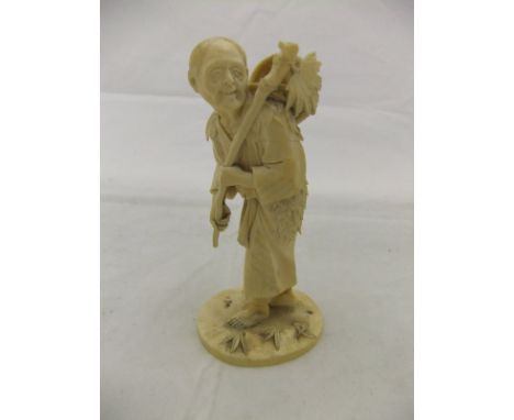 A Meiji period Japanese carved ivory okimono of an elderly gentleman carrying a stick and basket and wearing leaf covered clo