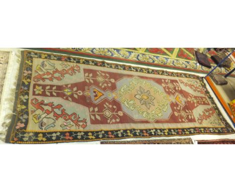 A Kelim rug, the central motif in pale blue, pale green, salmon, taupe and orange on a pale red stylised foliate decorated gr