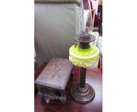 A Victorian oil lamp with a lime green glass reservoir and a metal column and base together with a small carved stool