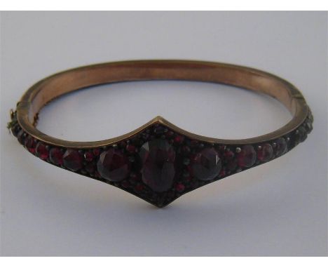 A Bohemian garnet hinged bangle, set over its entire length with stones, with three larger stones to the centre, 5.5cm inner 