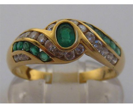 An emerald and diamond ring, the central oval cut emerald 4.5 x 3mm, in a surround of alternate bands of tension set emeralds