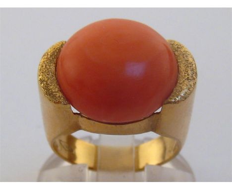 An 18 carat gold and coral ring, the circular domed stone 15.6mm diameter, the shank stamped ‘750’, finger size K, 10.2gms
