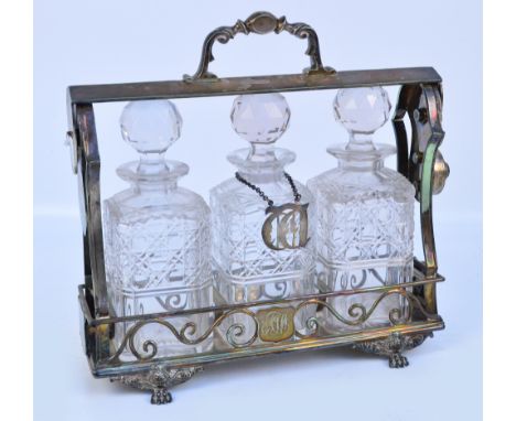 A silver plated three bottle tantalus with initialled shield shaped cartouche, raised on paw feet, the central cut glass deca