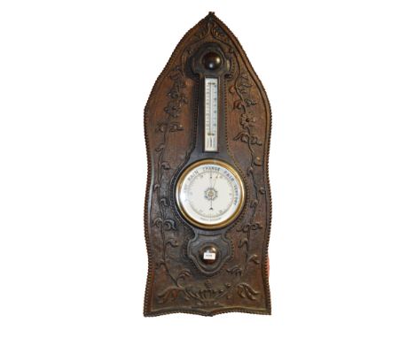 An Arts and Crafts oak aneroid barometer, mounted on a carved oak shield shaped back panel, height 109cm.