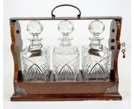 An Edwardian mahogany and electroplated tantalus by P B S, with central loop handle to the hinged lock release bar housing th