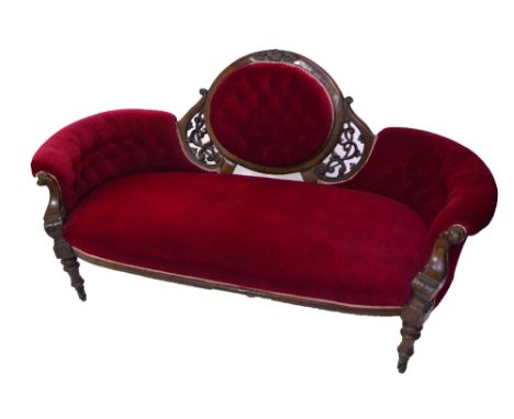 A Victorian mahogany framed upholstered sofa centred with a buttoned oval to the back, on ring turned front legs with castors