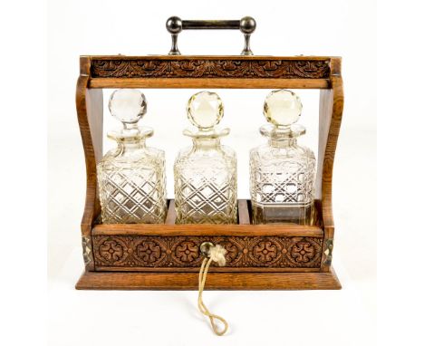 An Edwardian oak tantalus with carved acorn and floral motifs to the base and bar above three matched square sectioned clear 