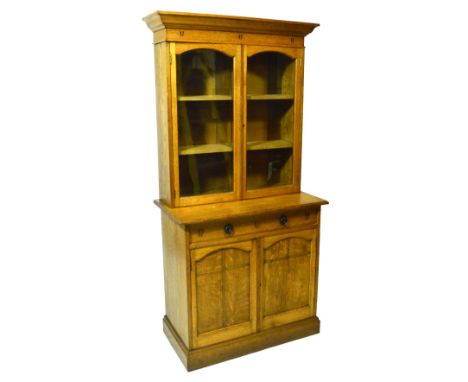 An Arts and Crafts oak bookcase on cupboard attributed to Archibald Taylor of Glasgow, the moulded cornice above two glazed d