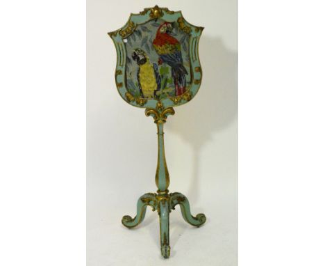 A carved floral and scroll decorated tripod fire screen with woolwork depicting two parrots within shield shaped glazed frame