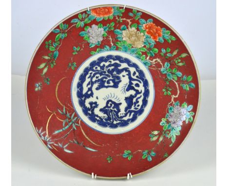 An early 20th century Japanese charger painted in underglaze blue to the centre within enamel border of flowers on iron red g