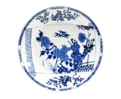 A Chinese blue and white porcelain charger, with open scroll decoration with peonies emerging from rocks and a fence, outer g