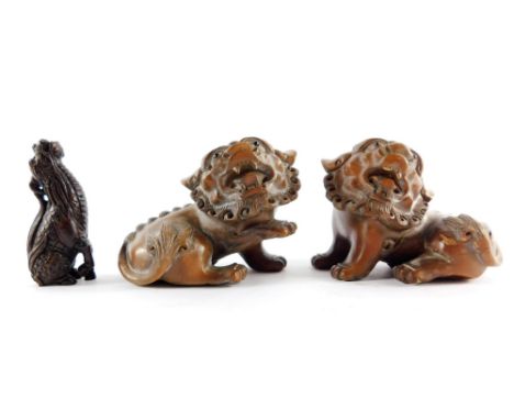 A pair of Chinese 19thC wooden carvings of dogs of fo, 8.5cm wide, and a Japanese carved wooden netsuke of a seated kirin, 7c