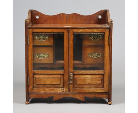An Edwardian oak pipe-smoker’s cabinet with a fitted interior enclosed by a pair of glazed &amp; fielded panel doors, 41.25cm