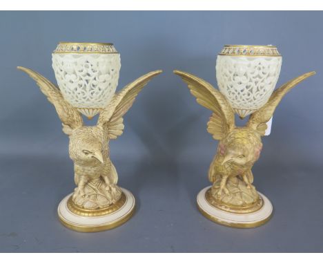 A pair of Royal Worcester ornaments in the form of birds holding a pierced basket on wings, raised on a circular plinth