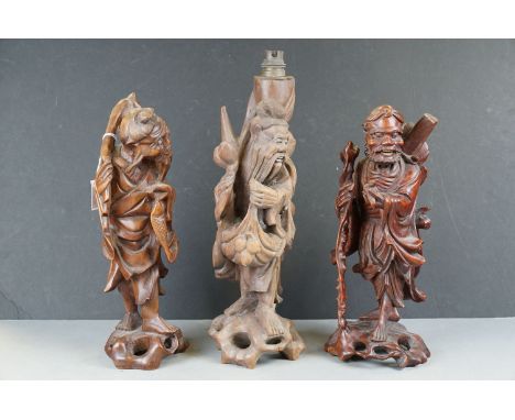 Two carved oriental wooden figures together with a similar table lamp. 