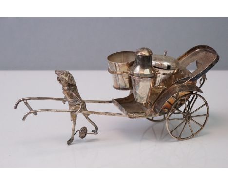 A vintage white metal cruet set in the form of an oriental figure pulling a rickshaw.