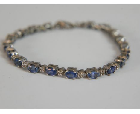 A silver sapphire and rough cut diamond tennis bracelet, set with nineteen oval mixed cut sapphires with a combined approxima