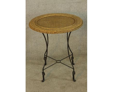 A vintage style wicker topped garden table raised on iron supports with 'X shaped stretcher. H.84 Dia.56cm. 