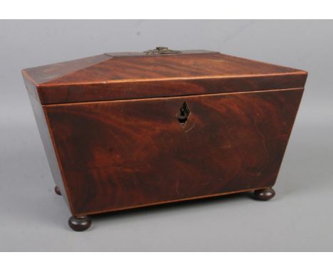 A mahogany tea caddy of sarcophagus form, raised on bun feet. The hinged lid revealing two sections and central slot for tea 