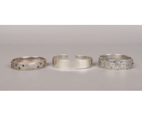 Three silver bangles including two chased examples, one set with garnets, 96 grams.Condition report intended as a guide only.