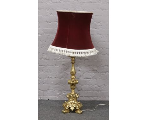 A large ornate gilt table lamp of candlestick form with burgundy fabric shade.