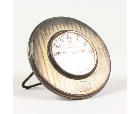 AN ENGINE TURNED SILVER CIRCULAR TRAVELLING CLOCK, with white enamel dial, stamped STERLING. 4.25ins diameter.