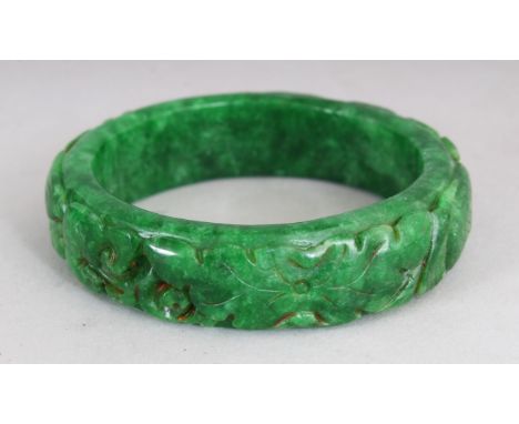 A CHINESE CARVED GREEN JADE BANGLE. 2.75ins diameter.