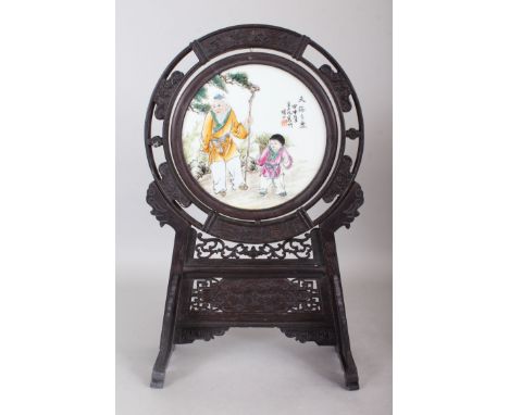A CHINESE CARVED HARDWOOD AND PORCELAIN TABLE SCREEN, the circular panel painted with an elderly man and young girl. 18.5ins 