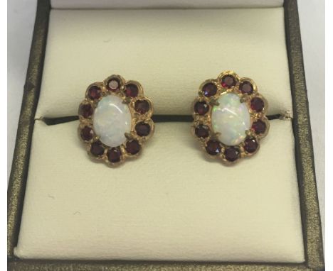 A pair of 9ct gold opal & garnet earrings. Central oval opals surrounded by a ring of garnets.